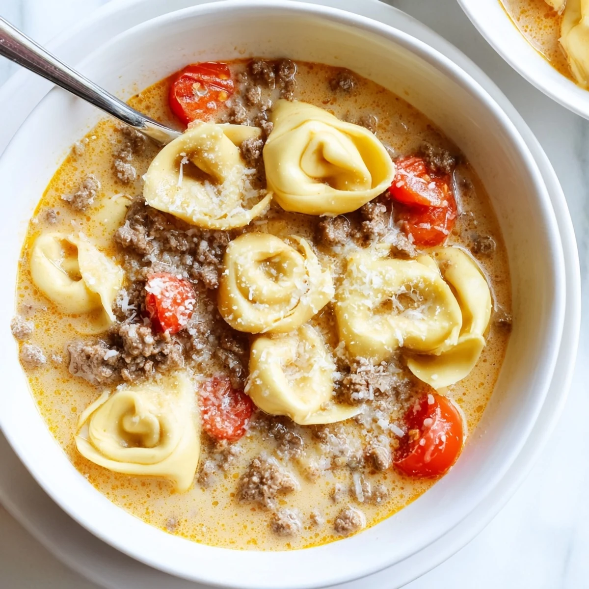 Savory Tortellini Beef Soup in a white bowl, garnished with fresh basil and Parmesan, next to a slice of crusty bread.