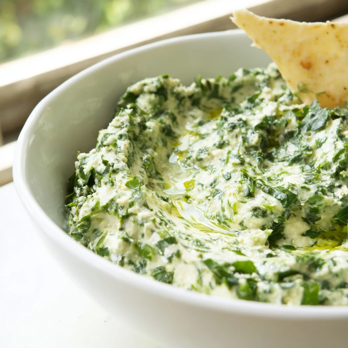 A close-up of creamy Green Goddess Salad Dip in a rustic bowl, garnished with vibrant green herbs and a drizzle of olive oil.