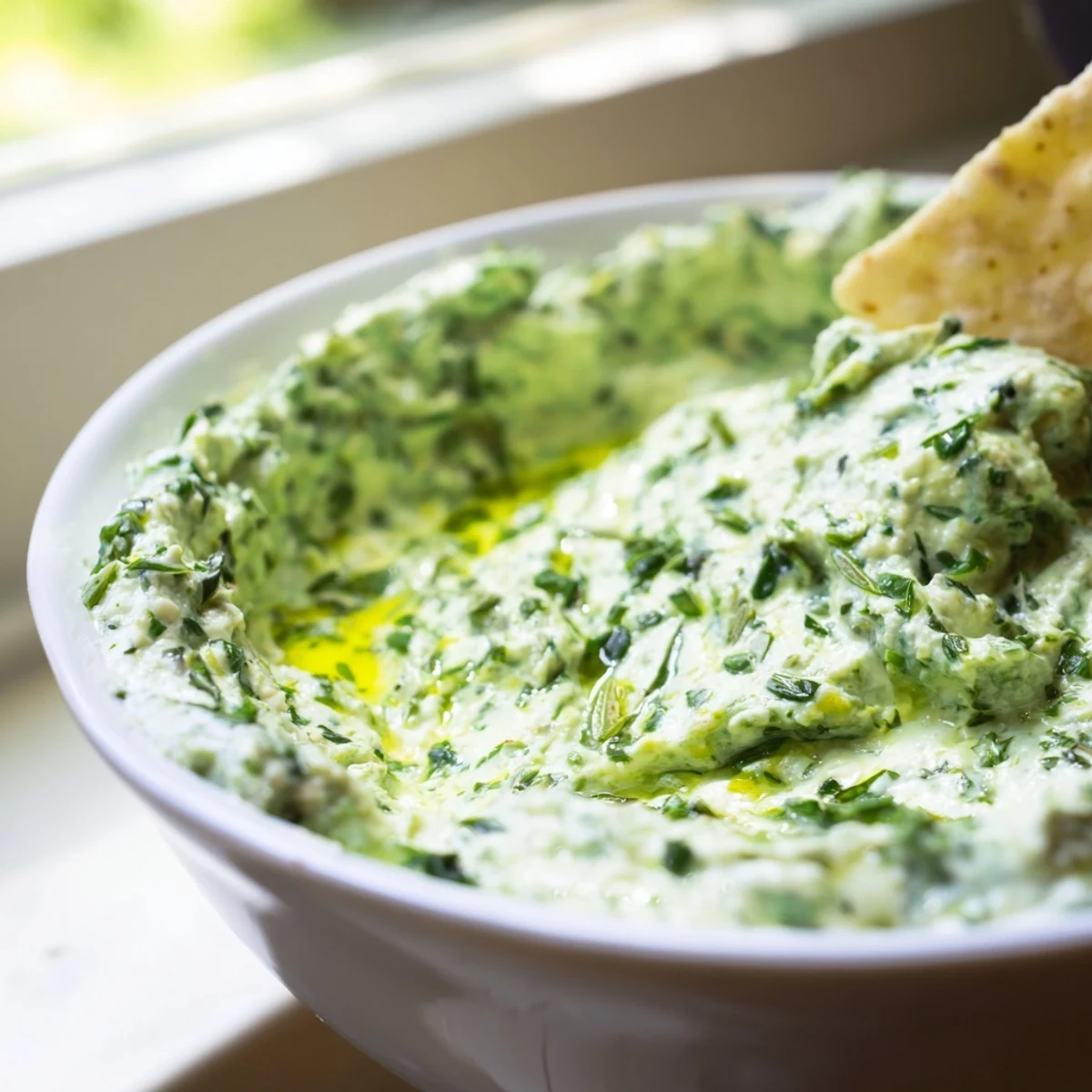 Plateful of crisp vegetable sticks and tortilla chips surrounding a bowl of fresh Green Goddess Salad Dip at a sunny picnic table.