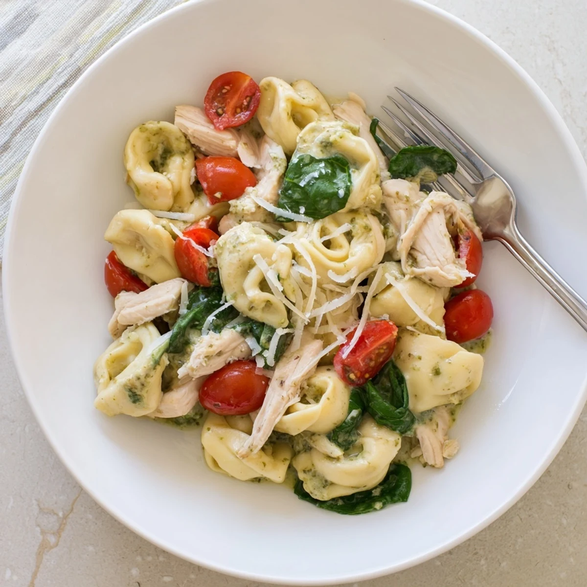 A close-up of creamy pesto tortellini skillet with rotisserie chicken, spinach, and cherry tomatoes.  