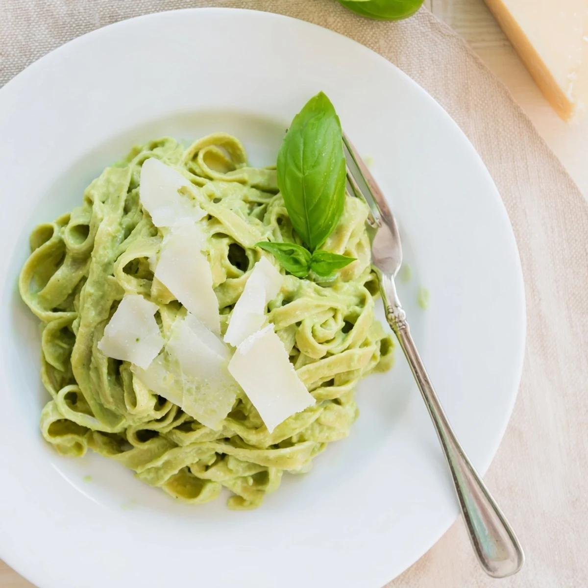 A bowl of Creamy Green Pea Alfredo pasta garnished with fresh basil, grated Parmesan, and cracked black pepper on a rustic wooden table.  