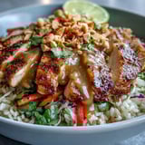 Colorful vegetable toppings including purple cabbage and carrots are piled on a warm Peanut Chicken Power Bowl.