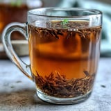 Steaming cup of Hojicha Americano with roasted Japanese green tea leaves in a rustic mug.