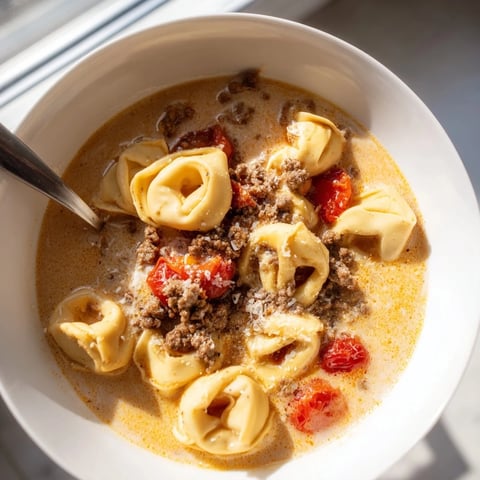 A bowl of creamy Tortellini Beef Soup with tender cheese-filled pasta, savory ground beef, and sweet cherry tomatoes in a rich broth.