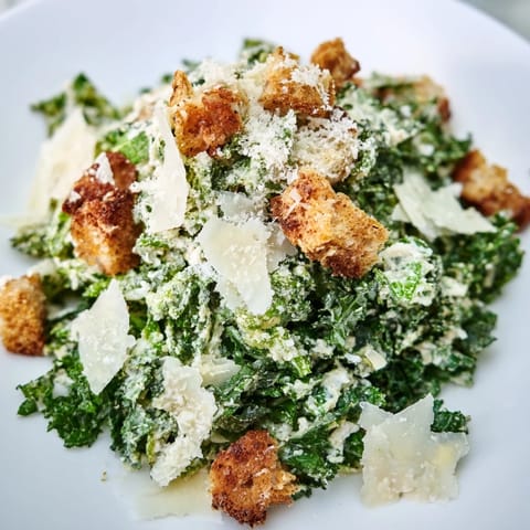 A bright image: a Kale Caesar Salad with shaved Parmesan and golden, crunchy croutons.