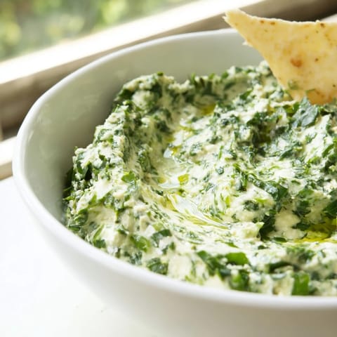 A close-up of creamy Green Goddess Salad Dip in a rustic bowl, garnished with vibrant green herbs and a drizzle of olive oil.