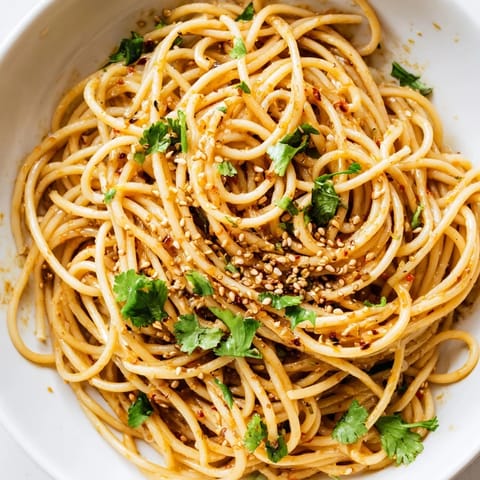 A vibrant bowl of Spicy Sesame Noodle Salad, featuring julienned cucumbers, scallions, and chopped peanuts for a crunchy, refreshing bite.