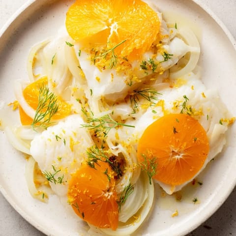 Fresh fennel fronds and vibrant orange slices garnish this poached cod, served steaming hot in a shallow bowl for a comforting family meal.  