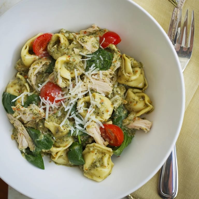Steaming creamy pesto tortellini skillet in a cast-iron pan, garnished with fresh basil and Parmesan.  
