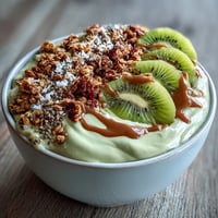 Creamy hojicha smoothie bowl topped with granola, fresh berries, and sliced kiwi on a marble counter.