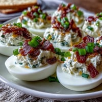 Jalapeño Popper Deviled Eggs with crispy bacon and cream cheese filling, garnished with fresh jalapeño slices.